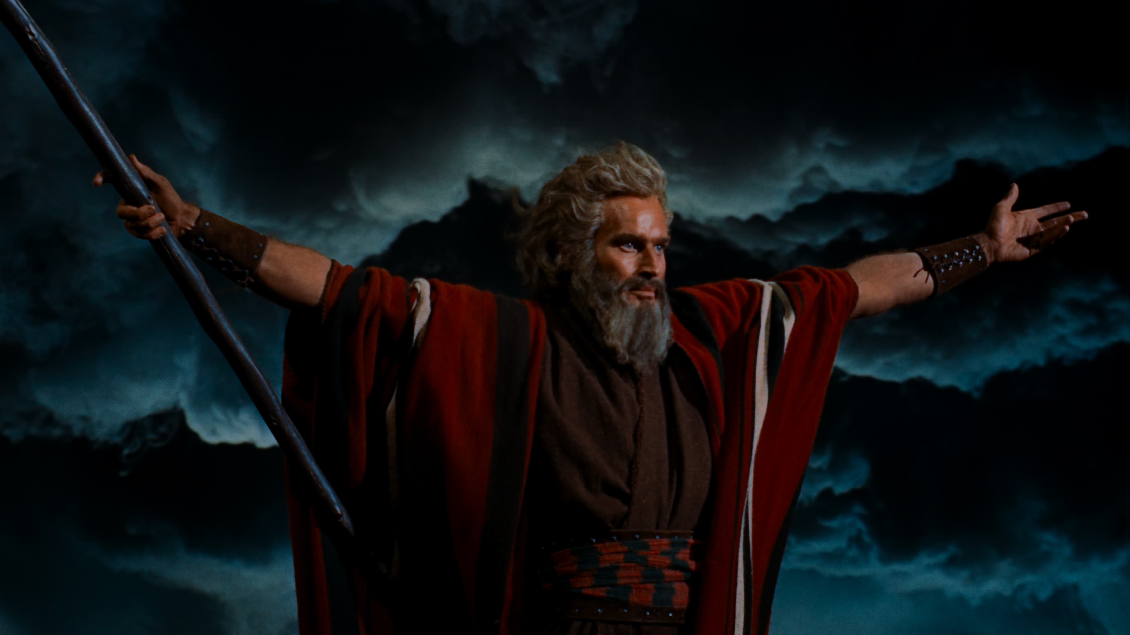 a man with outstretched arms in front of a wall of clouds